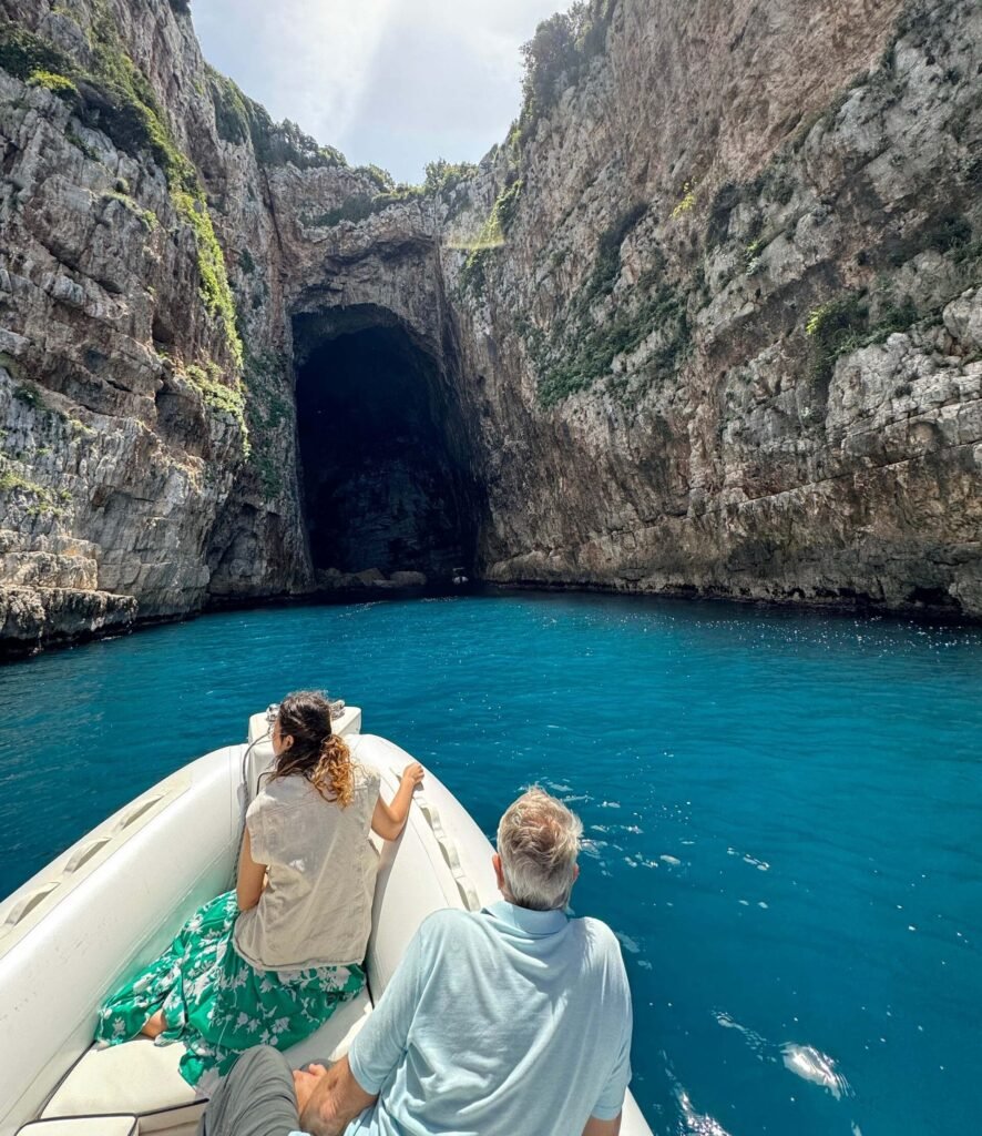 Exploring Haxhi Ali Cave in Karaburun, Albania – a breathtaking sea cave with towering limestone cliffs, crystal-clear blue waters, and a rich history. Visitors on a boat tour admire the stunning natural wonder, a must-visit destination on the Albanian Riviera.