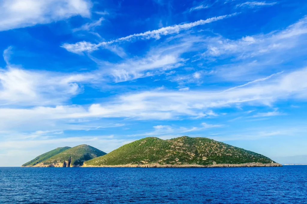 A breathtaking view of Sazan Island, Albania, captured from the side, showcasing its rugged coastline, crystal-clear waters, and lush Mediterranean landscape. Sazan Island, the largest island in Albania, is a hidden gem in the Adriatic Sea, offering rich history, untouched nature, and stunning panoramic views.
