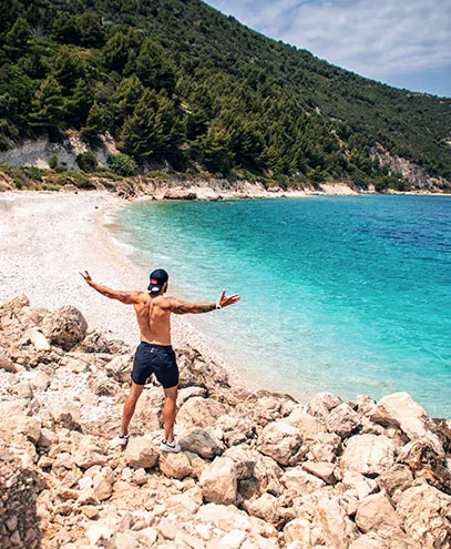 A man stands atop rocky terrain on Sazan Island, Albania, with his arms wide open, embracing the breathtaking coastal scenery.