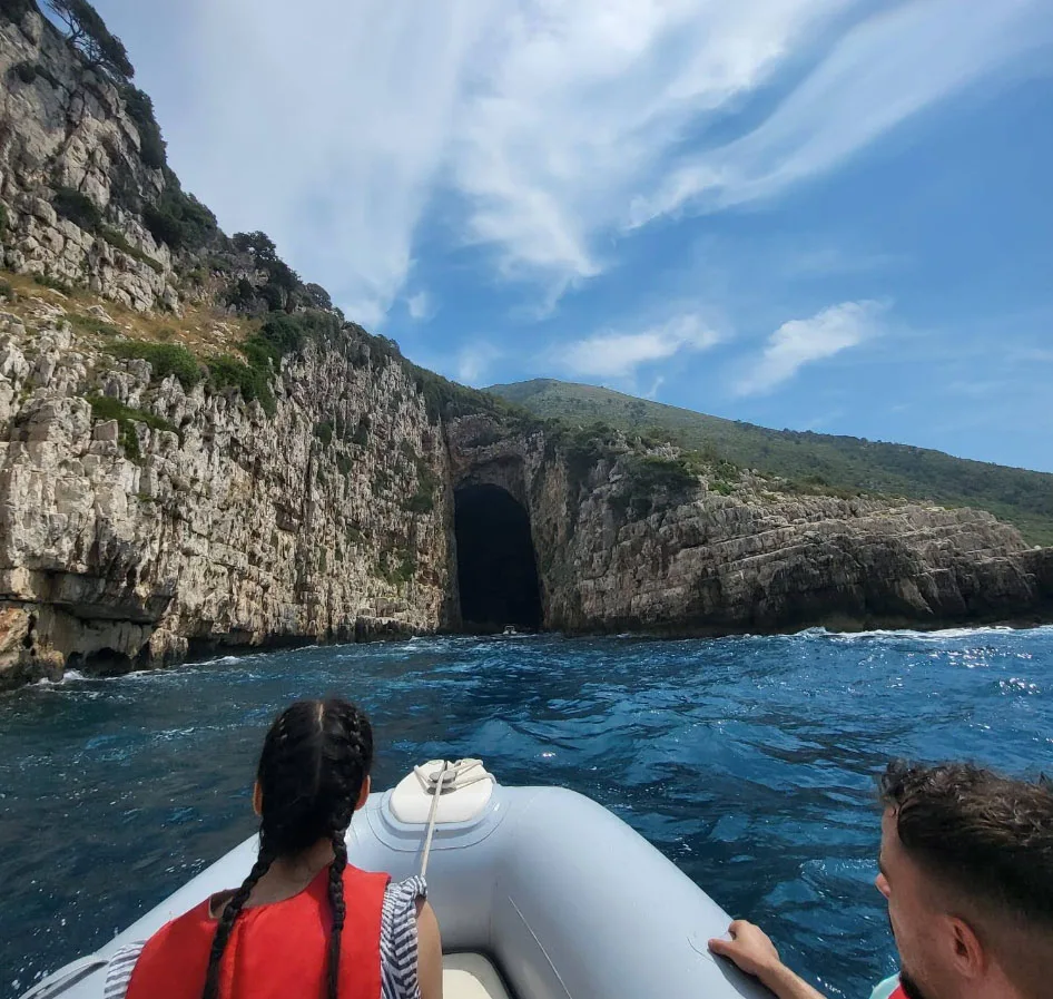 Speedboat approaching the entrance of Haxhi Ali Cave, a stunning sea cave on the Albanian Riviera near Sazan Island. Towering limestone cliffs covered in lush greenery surround the massive cave, which is a popular destination for boat tours, snorkeling, and exploring Albania’s hidden coastal gems.