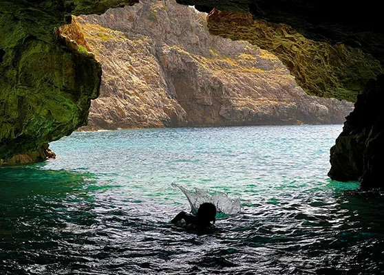 A woman swimming inside Dafina Cave, Albania, surrounded by stunning turquoise waters and framed by rugged limestone formations.