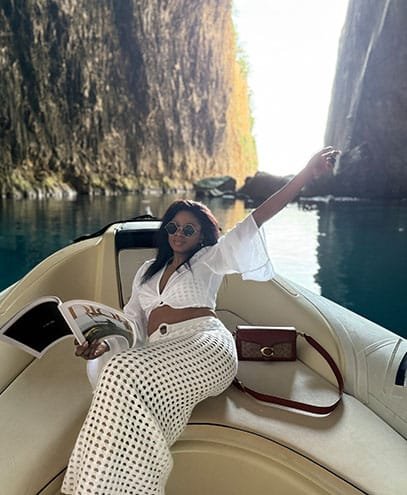 A fashionable woman lounging on a boat within Haxhi Ali Cave, Albania, embraced by mesmerizing turquoise waters and glowing limestone formations.