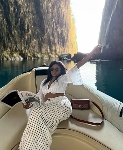 A fashionable woman lounging on a boat within Haxhi Ali Cave, Albania, embraced by mesmerizing turquoise waters and glowing limestone formations.