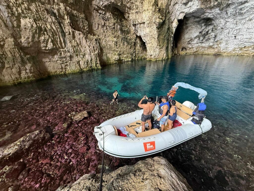 A speed boat, inside Haxhi Ali Cave. People are swimming inside, azure waters can be seen.